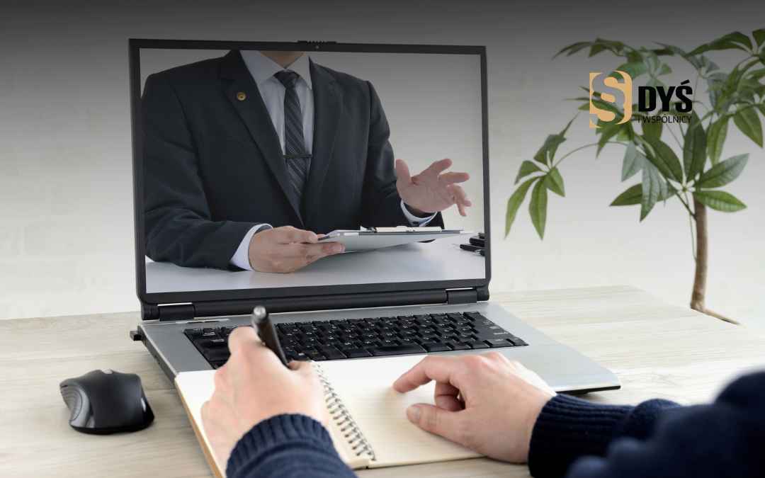 Klient robi notatki na biurku podczas konsultacji z prawnikiem widocznym na ekranie laptopa.