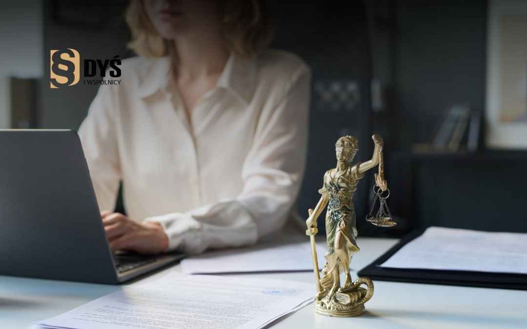 Prawnik analizuje umowę kredytową przy laptopie obok statuetki Temidy.