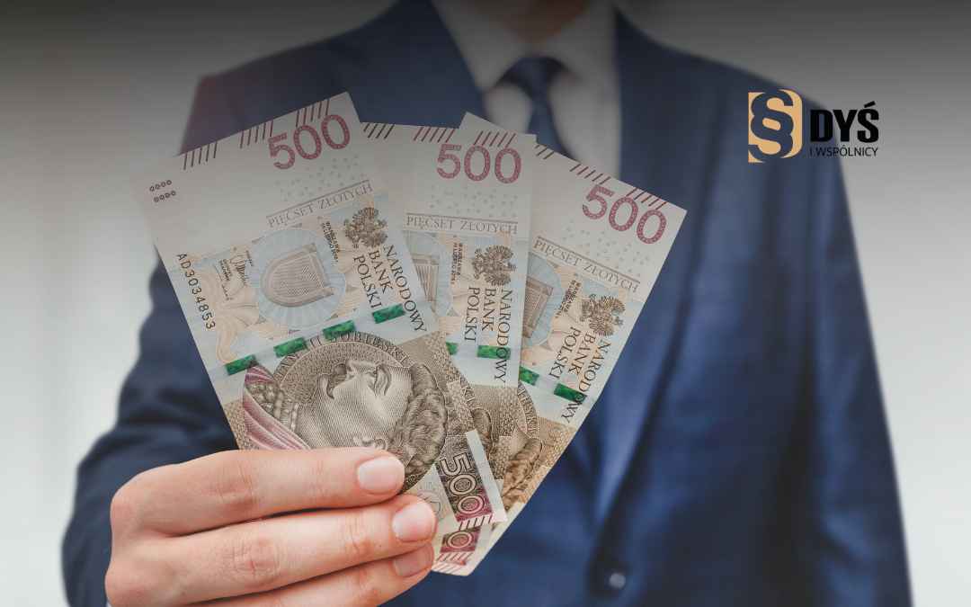 Mężczyzna w garniturze trzyma banknoty 500 zł.