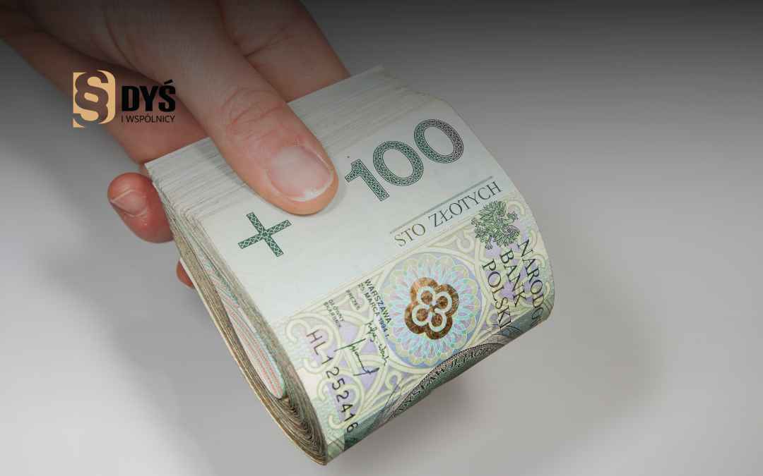 Dłoń trzyma zwinięty plik polskich banknotów stuzłotowych.
